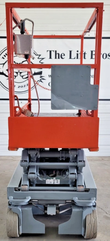 Red guardrail platform lowered on the folded scissor stack, gray chassis, solid wheels, chain across the entry gate