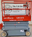 Skyjack SJIII 3219 scissor lift lowered, red guardrail platform with slide-out deck, gray chassis on four solid wheels