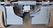 Underside of the steer axle: hydraulic steering cylinder, tie rods and lowered pothole guards between solid tires