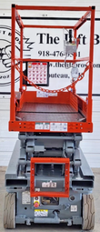Rear of the lowered Skyjack scissor lift: orange guardrails and entry chain above the gray chassis and solid tires