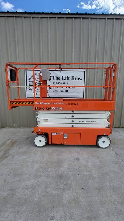 Orange 2019 Snorkel S3226E electric scissor lift, stowed, side view in front of the Lift Bros sign