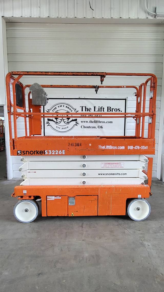 Orange Snorkel S3226E scissor lift, lowered, side view of the platform, white scissor stack and non-marking wheels