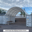 White single-pipe arched shelter spanning two white shipping containers, workbench beside it