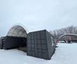 White PVC container shelter roof arched over two dark shipping containers, open end facing the camera