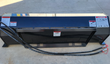 Black skid steer tiller front-on: quick-attach mount plate with warning decals, rotor housing and coiled hydraulic hoses