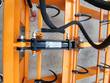 Black hydraulic cylinder bolted to the orange accumulator frame, braided hoses and a warning decal