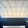 Underside of a container shelter: galvanized arch tubes, ratchet tensioners and an AC unit on the dark container wall