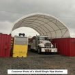 White arched shelter between two red shipping containers with a white service truck parked inside