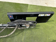 Sickle bar mower's black quick-attach plate with Wolverine decal, hazard labels, tilt cylinder, hoses and valve block