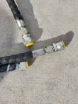 Two hydraulic supply hoses in black spiral wrap, steel couplers capped with yellow dust plugs