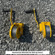 Yellow mechanical roll-up door winches with hand cranks and cable, laid on gravel