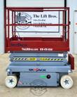 Skyjack scissor lift lowered, upper control box on the red platform rail, KEEP CLEAR striping on the scissor stack