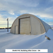 Arched building with metal-panel end wall, overhead door and entry door, PVC cover over the roof, snowdrifts around it