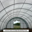 Inside a fabric building looking out the open end door, arched ribs overhead and a pasture beyond
