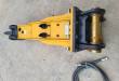 SB40 breaker from above: black top-mount bracket with brass pivot pin, chisel fitted, hoses coiled