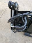 Clamshell cylinder and pivot at the 4-in-1 bucket's corner, sleeved hose runs looped over the frame