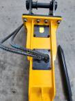 Top of the yellow TOFT750 breaker: bolted valve covers, caution decal, hydraulic hoses and a spare chisel
