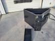 Concrete bucket with gate housing and hydraulic hose coiled at the side, pour chute on the ground