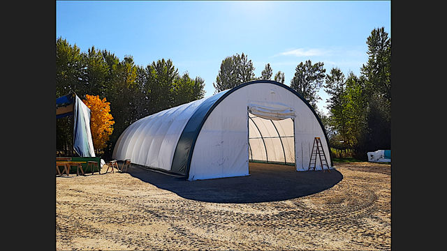 White fabric building with dark green trim and open door, ladder out front