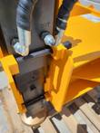 Post driver hydraulic ports marked IN and OUT with 90-degree fittings and connected hoses