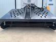 Gray hydraulic landscape rake, slotted debris hopper deck over a tined raking drum, hydraulic hoses at the mount