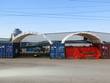 Two white container shelters installed across shipping containers, sheltering stored pallets and equipment