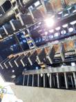 Underside of the landscape rake: drive chains and rows of angled steel scoop teeth on the drum, perforated grate above