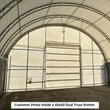 Inside a dual-truss shelter: arched galvanized trusses over a roll-up door end wall on a concrete floor
