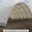 White single-pipe arched shelter on a corrugated metal pony wall, open end showing pipe ribs over gravel