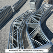 Galvanized steel dual-truss frame parts staged on gravel, labeled "50x100 Dual Truss Building"