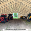 Inside a tan dual-truss fabric building, tractors, skid steer, boom lift and excavator parked along the walls