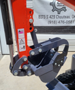 MX15RX digging bucket and fixed thumb linkage on the orange boom arm, with pinch-point warning decals