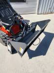 4-in-1 bucket held level on an orange mini skid steer, serrated jaw edge running the full width