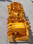 Yellow attachment package lengthwise on the pallet: rows of grapple and rake tines, buckets and auger bit