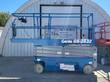 Blue Genie GS-2632 electric scissor lift, side view, lowered, beside a red Skyjack lift