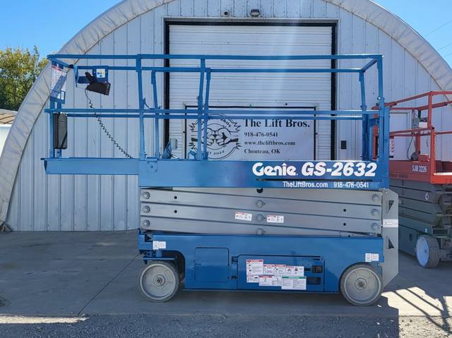 Blue Genie GS-2632 electric scissor lift, side view, lowered, beside a red Skyjack lift