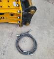 Rear of the SB40 breaker with black mount and brass pins, coiled hydraulic hose pair alongside