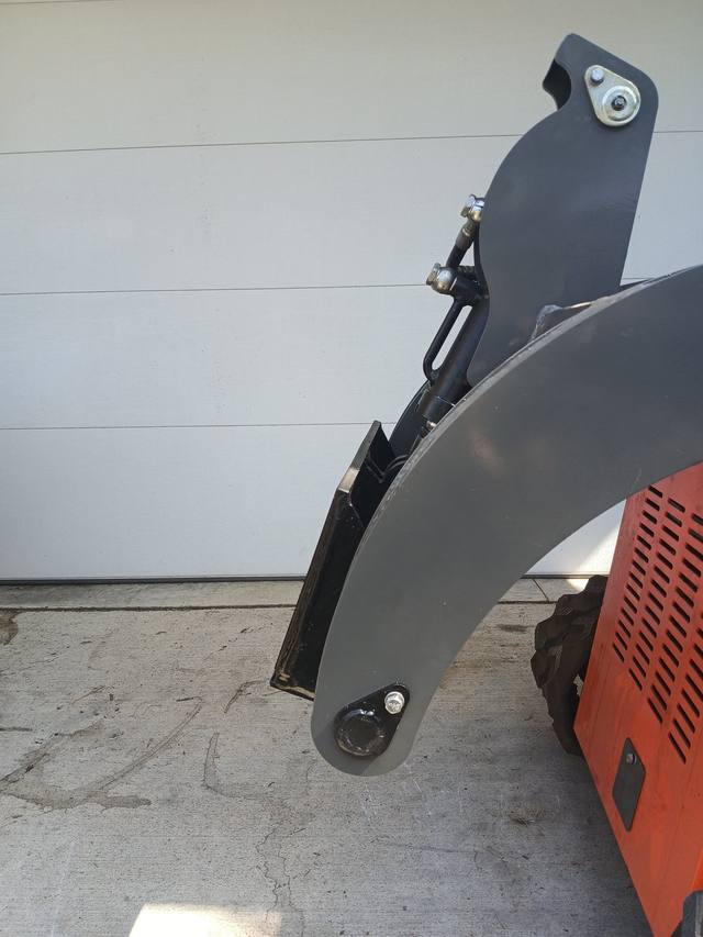 Black quick attach plate mounted on the gray lift arms of an orange mini skid steer