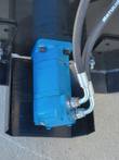 Blue hydraulic drive motor bolted to the black tiller frame, twin hoses with steel elbow fittings at its ports
