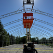 Galvanized steel dual-truss fabric building frame going up, orange JLG boom lift raised inside among the bare arches