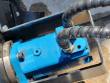 Blue hydraulic drive motor bolted into the broom frame, two braided hoses connected to its ports