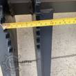 Grapple bucket steel tines from below, tape measure gauging the spacing between the bars