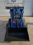 Blue AGT MX-MRW14 mini skid steer head-on, black bucket lowered, red auxiliary hydraulic couplers and knobby tires