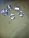 Six machined steel cylinder pin bushings scattered, sides and bores visible