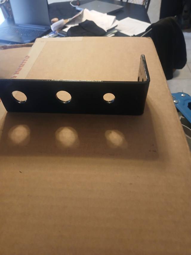 Auxiliary hydraulic line bracket, black steel angle with three coupler holes