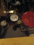 Hydraulic filter gauge, 0 to 30 psi dial, installed on the filter housing of a yellow mini skid steer