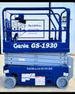 Genie GS-1930 scissor lift in blue, platform lowered with guardrails up, hand controller on the rail, solid tires