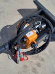 Auger drive's orange gearbox and motor with sleeved hydraulic hoses and red-capped quick couplers
