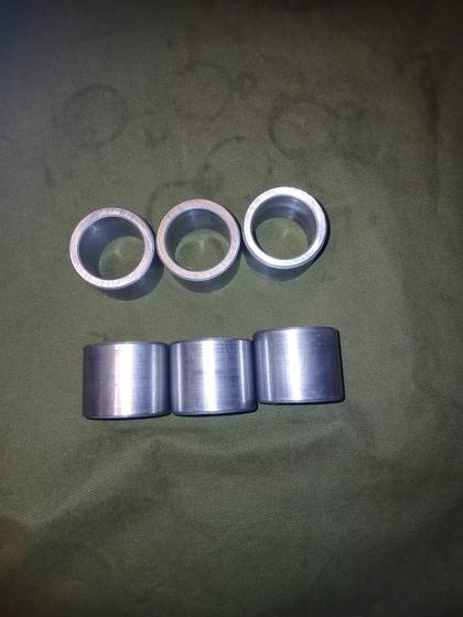Six steel cylinder pin bushings, three showing bores and three showing machined sides