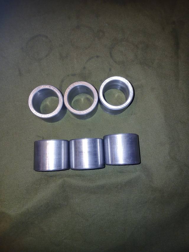 Six steel cylinder pin bushings, three showing bores and three showing machined sides